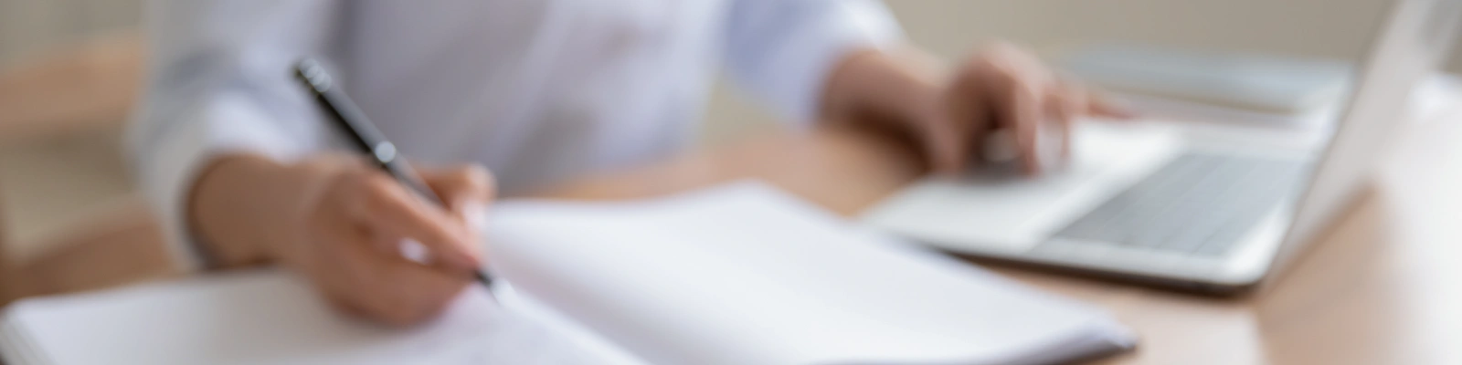 person writing in a notepad whilst typing on a laptop